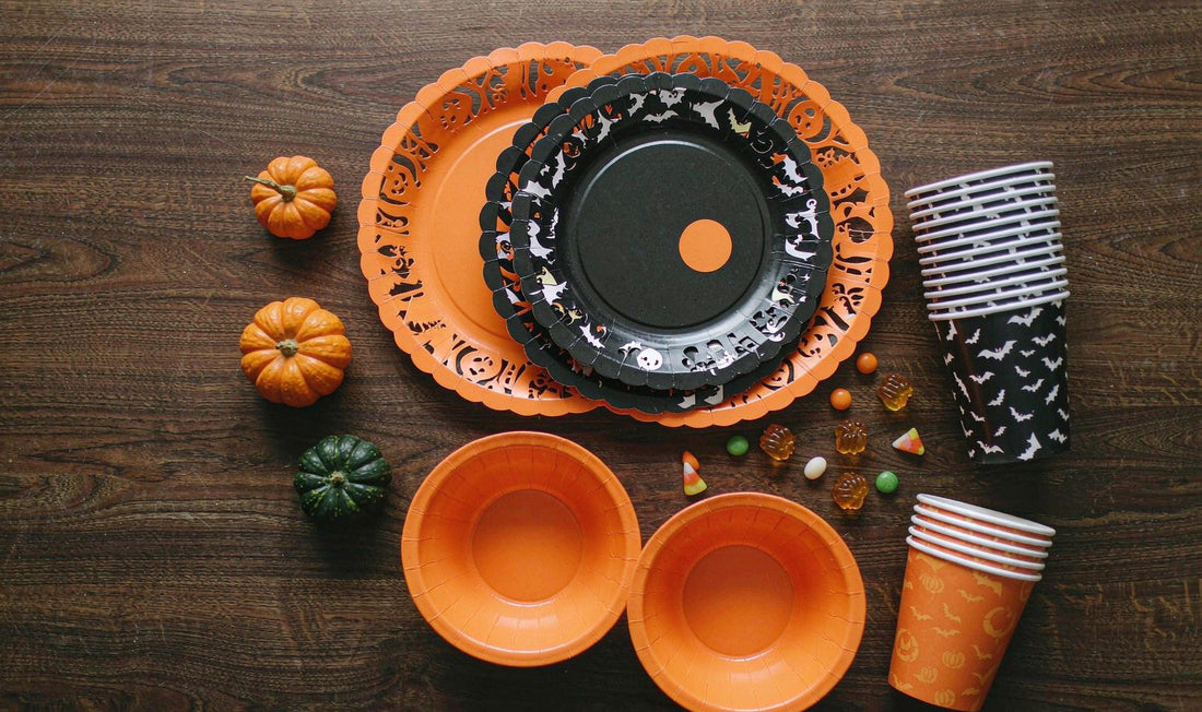 Halloween paper plates, napkins, and cups arranged on a dark table with pumpkins
